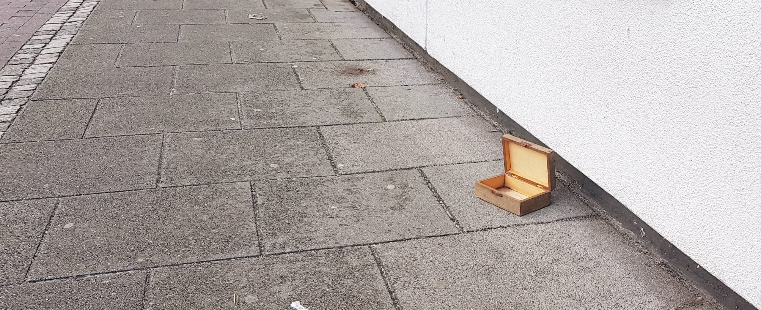 aufgeklapptes Holzkästchen liegt auf dem Bürgersteig