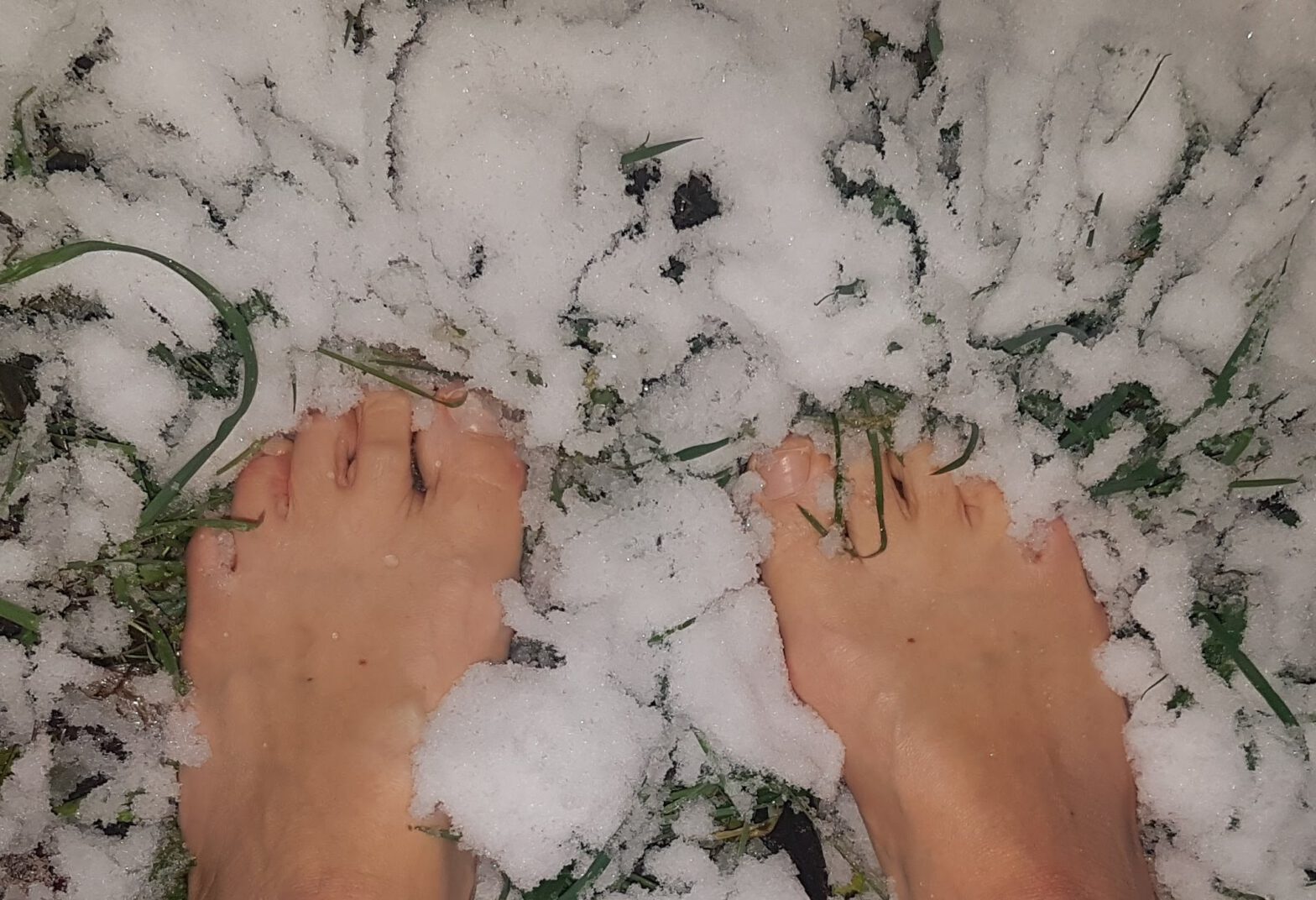 Nackte Füße in frischem Schnee auf Gras, Blick von oben